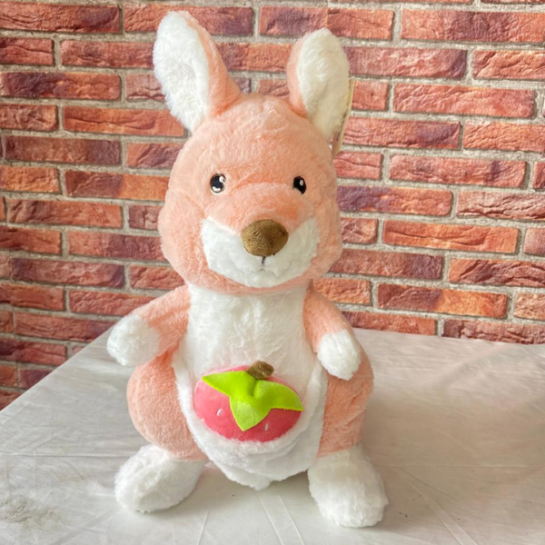 Plush toy kangaroo with a green leaf and red fruit against a brick wall background