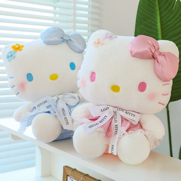 Two Hello Kitty plush toys, one in blue and one in pink, on a white surface with a blurred background.